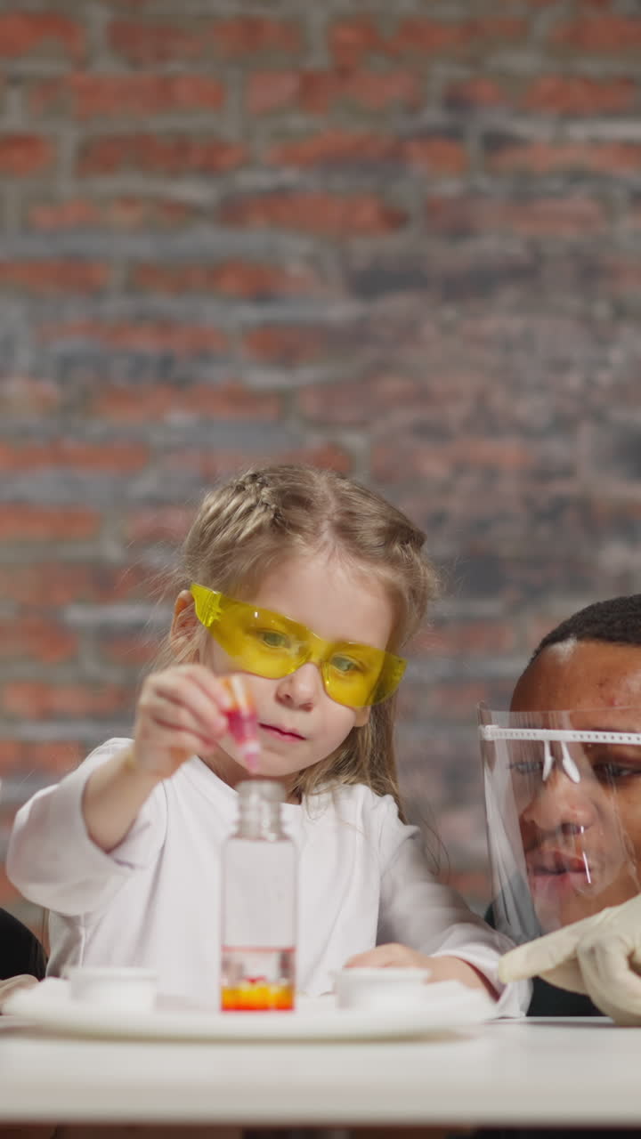 Little girl student looks at changing color paint providing chemical experiment with careful teachers at fun lesson in scientific laboratory