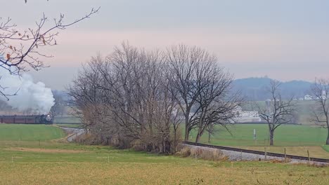 A-View-of-an-Antique-Steam-Passenger-Train-Approaching,-Puffing-Lots-of-Steam-Traveling-Through-the-Countryside-on-a-Winter-Day