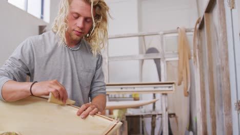A-Caucasian-male-surfboard-maker-polishing-a-wooden-surfboard-edge