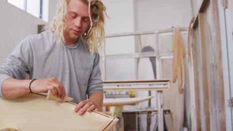 a caucasian male surfboard maker polishing a wooden surfboard edge