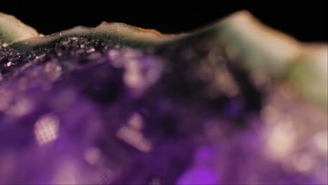 Close-up-cinematic-pan-of-purple-amethyst-crystal-and-crust-lit-on-black-background,-with-reflection-below