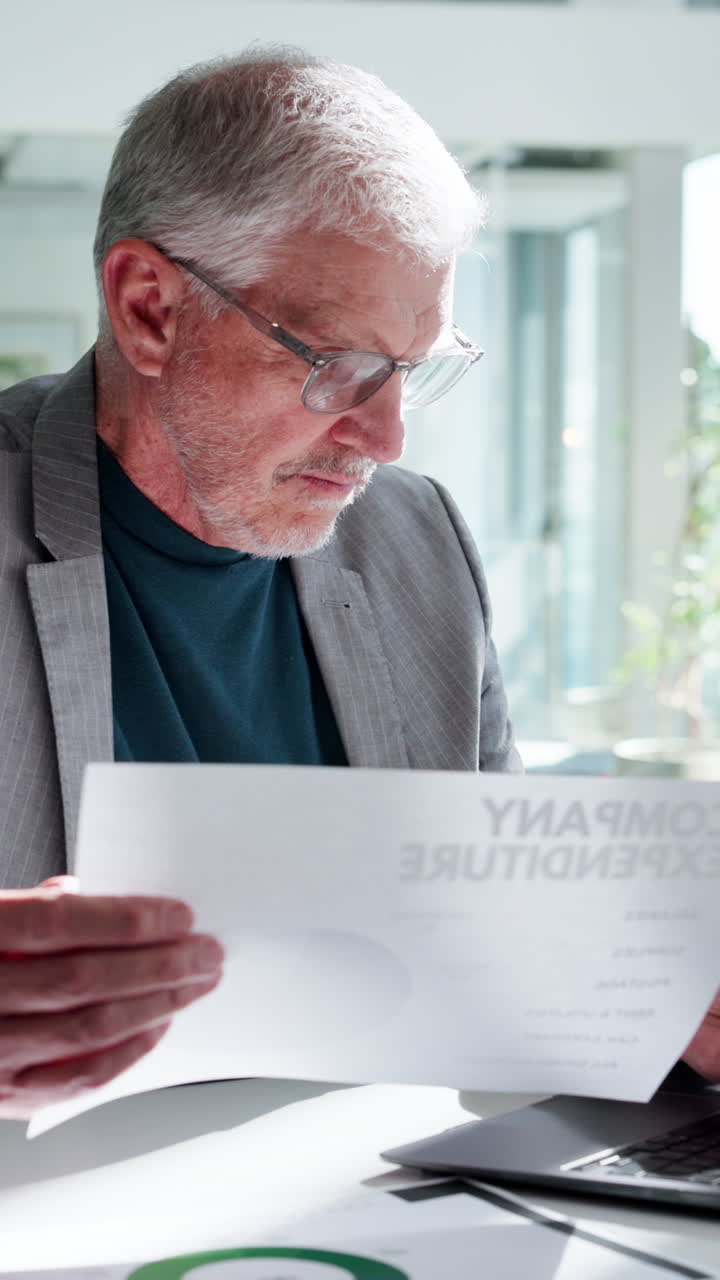 Empresario sénior revisando documentos y trabajando en un portátil
