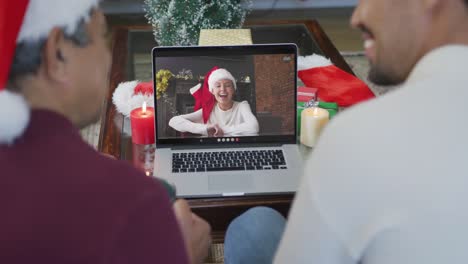 Padre-E-Hijo-Birraciales-Sonrientes-Usando-Una-Computadora-Portátil-Para-Una-Videollamada-Navideña-Con-Una-Mujer-En-La-Pantalla