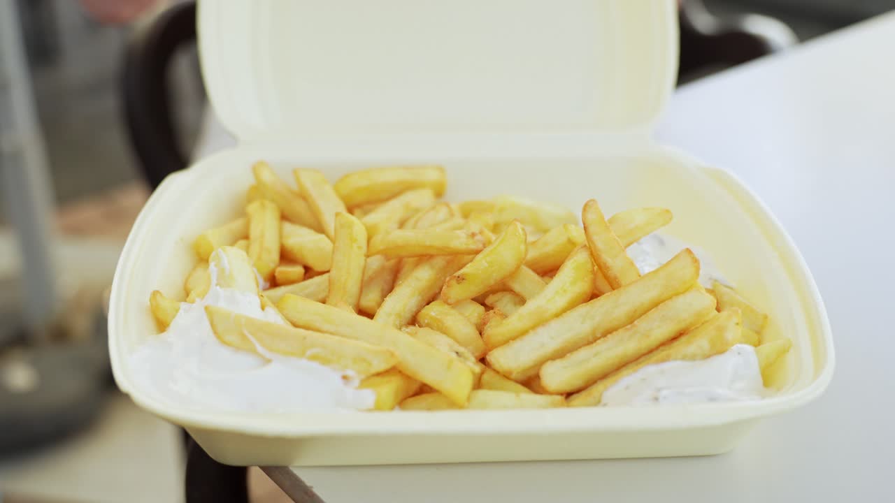 Picking up french fries and dipping them in mayonnaise on disposable disposable clamshell container, static closeup
