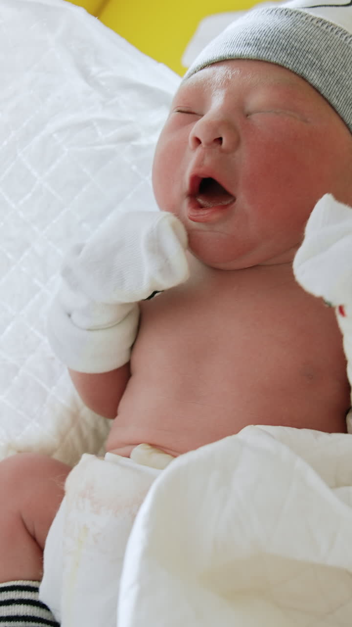Tiny newborn baby in hat and mittens. Child in a wrap is taken into hands. Close up. Vertical video