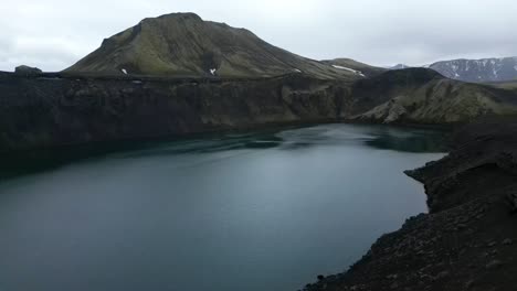 Aerial-view-from-Blahylur-crater-lake-in-the-Highlands-of-Iceland-during-summer,-surrounded-by-greens-and-greys-forms,-beautiful-mountains-and-dark-roads