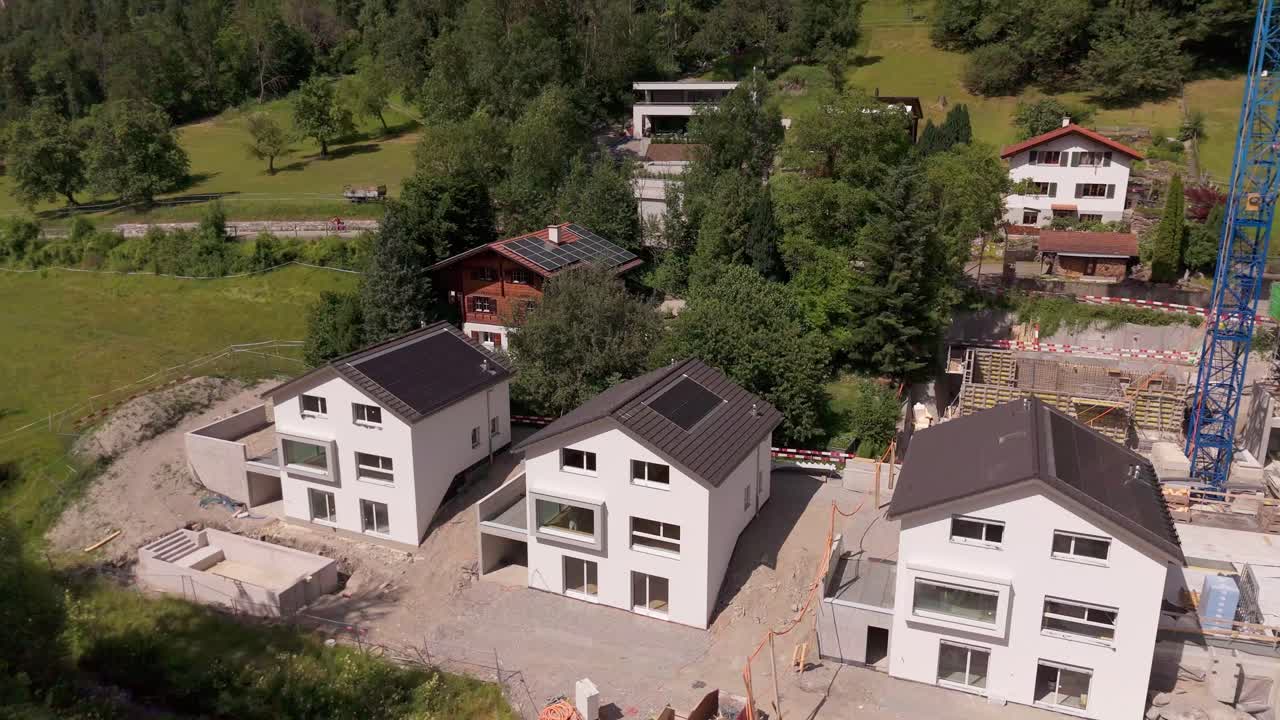 Eneboliger i sveitsisk by under byggefasen. Byggeplass med kran i Alpene. Solrik sommerdag. Luftfoto tatt bakover.