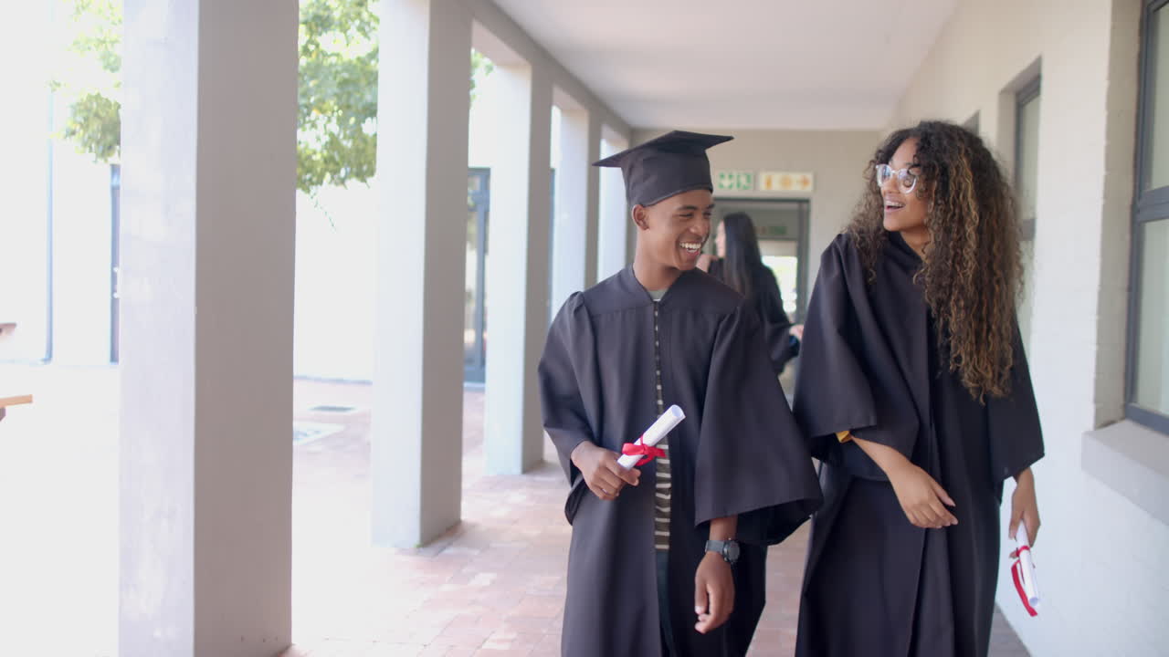 Biracial graduates walk through high school corridors, with copy space