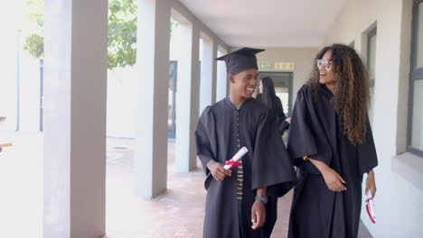 biracial graduates walk through high school corridors, with copy space