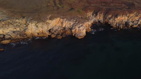 Drone-top-down-aerial-view-of-waves-splash-against-rocky-seashore,-background