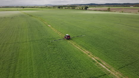 tractor operating a continuous spray machine containing agrochemicals on a farm aerial shot