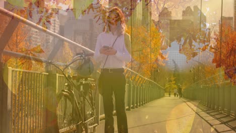 animation of autumn leaves falling over caucasian man with bike using smartphone