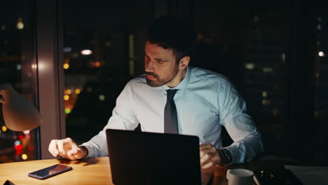 late office worker sitting dark workplace with laptop closeup. businessman tired