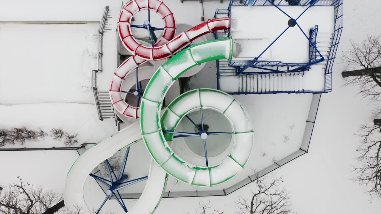 aéreo de arriba hacia abajo, toboganes de agua vacíos cubiertos de nieve en una piscina durante la temporada de invierno