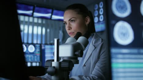 medical research scientist looking under the microscope in the laboratory. neurologist solving puzzles of the mind and brain. in the laboratory with multiple screens showing mri / ct brain scan images.