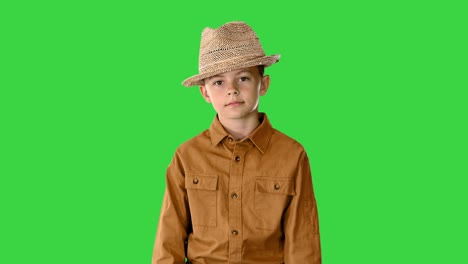 boy in a shirt and straw hat walking waving his hands and looking at camera on a green screen, chroma key