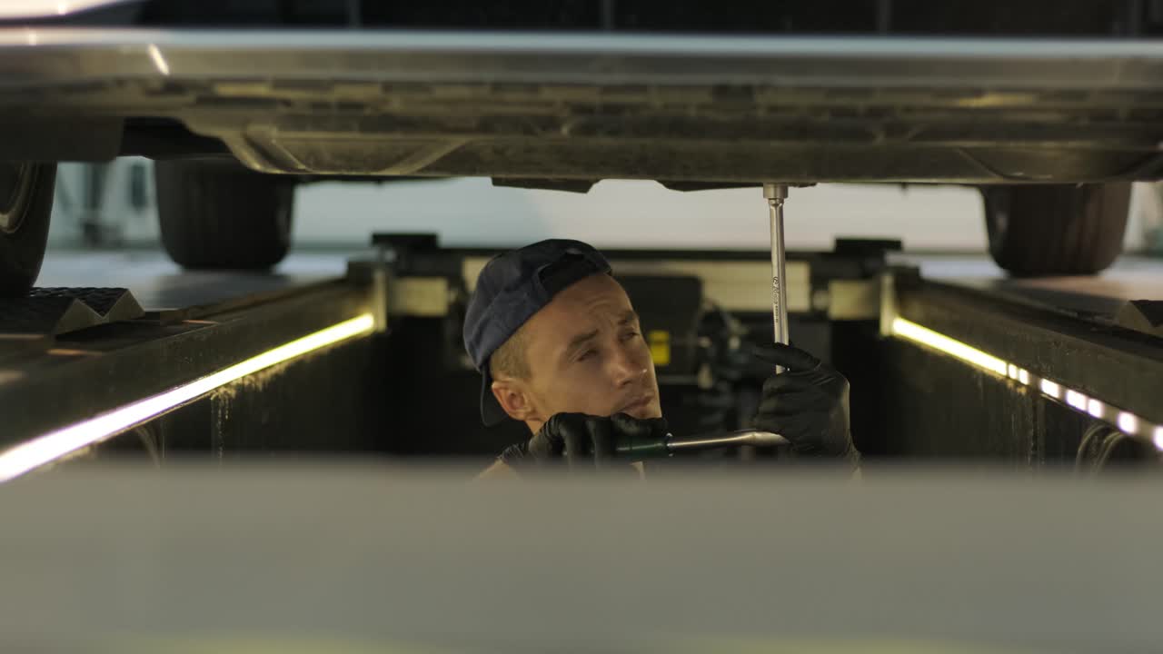 mecánico de automóviles que trabaja debajo de la máquina de elevación de automóviles en el garaje. taller de reparación de autos, servicio de automóviles, reparación.