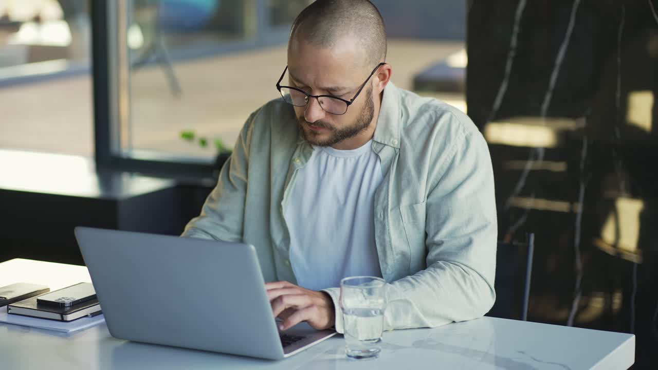 hombre de negocios motivado con gafas trabajando en una computadora portátil y tomando un sorbo de agua