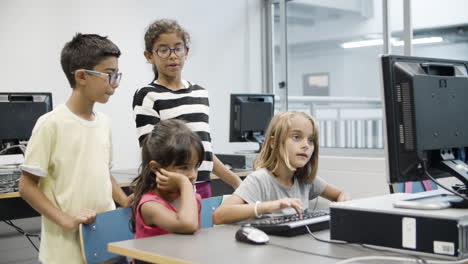 Blonde-girl-yping-on-keyboard-while-classmates-watching-at-the-monitor-and-talking