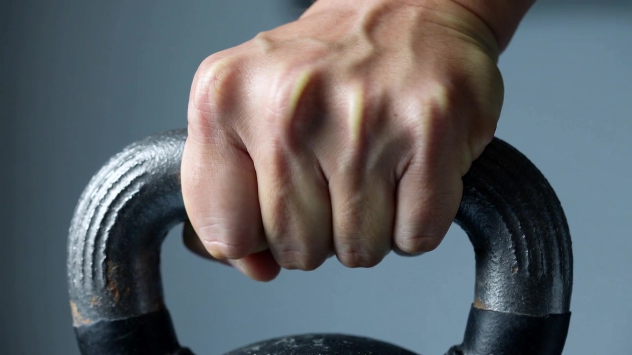 Gripping single adult hand maintaining firm hold at gym, preparing for lift with kettlebell