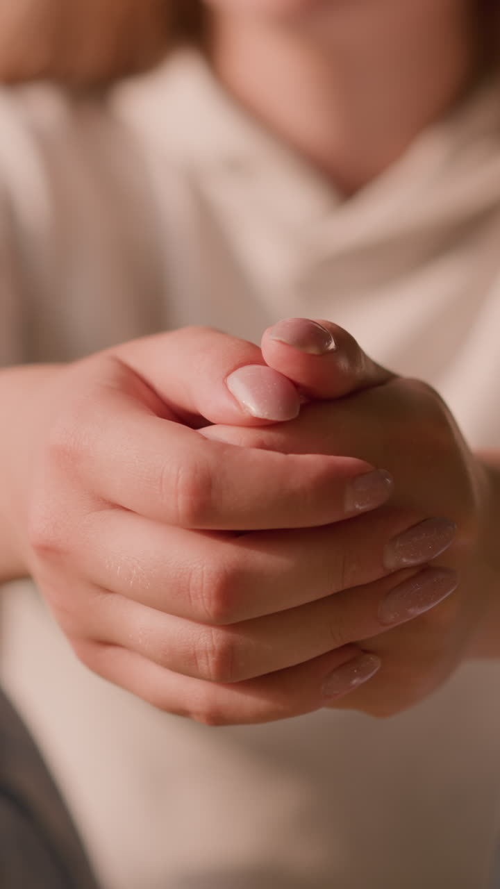 joven se sienta con las manos juntas, expresando calma e introspección en medio de un fondo borroso de vegetación exuberante y una figura débil en azul