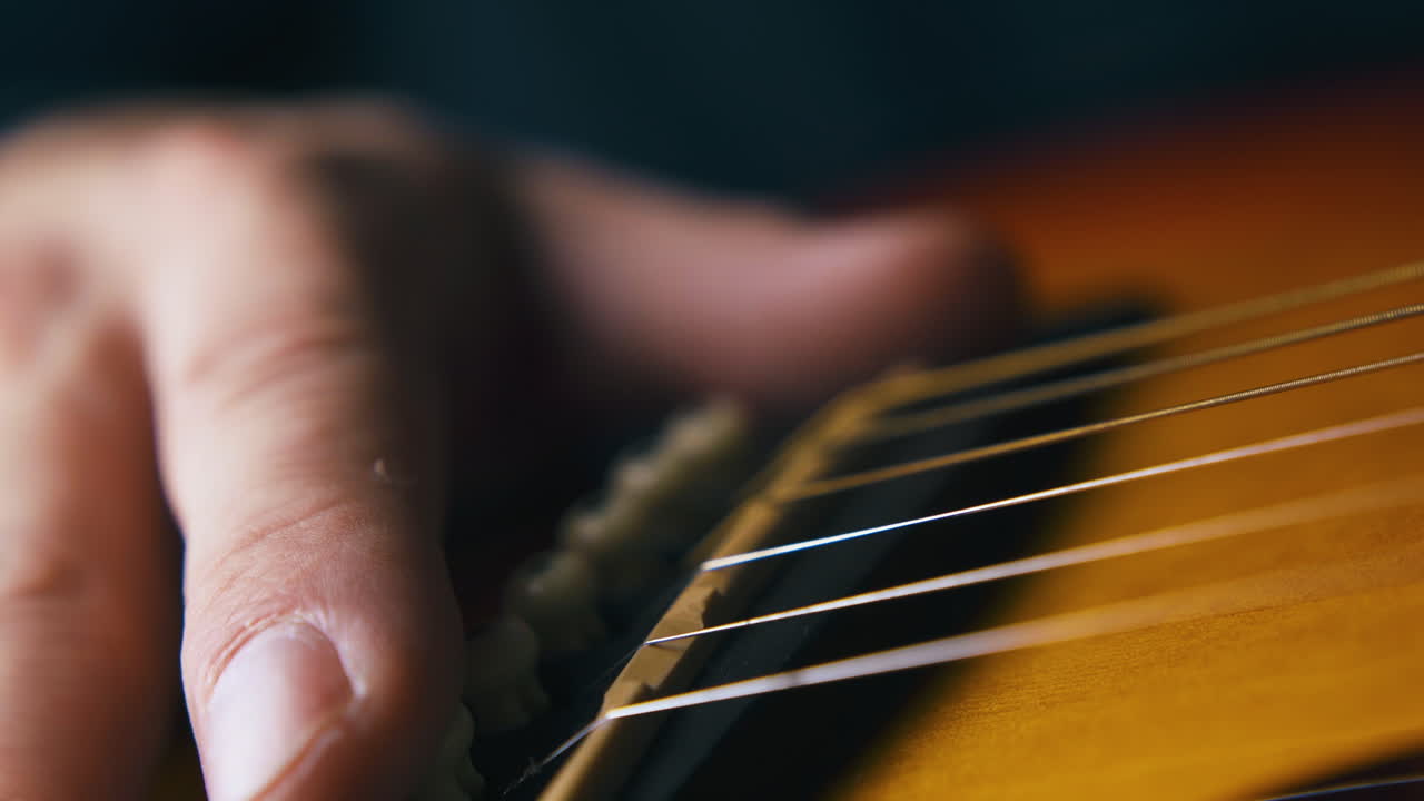 musician holds hand on brown acoustic guitar body closeup