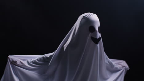 child dressed up in ghost costume trick or treating at halloween scaring people in front of black studio background