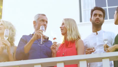 Friends-interacting-with-each-other-while-having-champagne-in-balcony