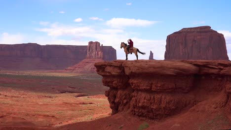 a cowboy sits on a horse on a cliff in monument valley utah 1