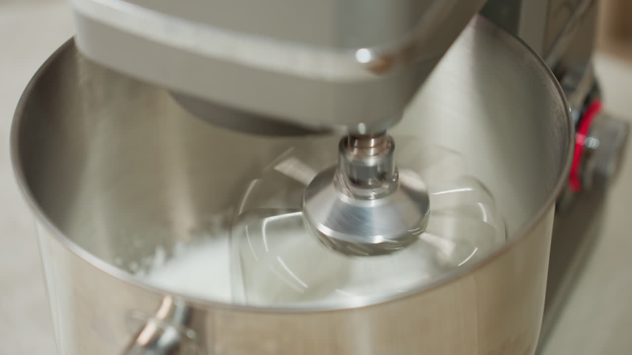 Close up of electric stand mixer whipping mashed white ingredient inside metallic mixing bowl on kitchen counter, showing rapid movement of whisk attachment blending mixture for baking