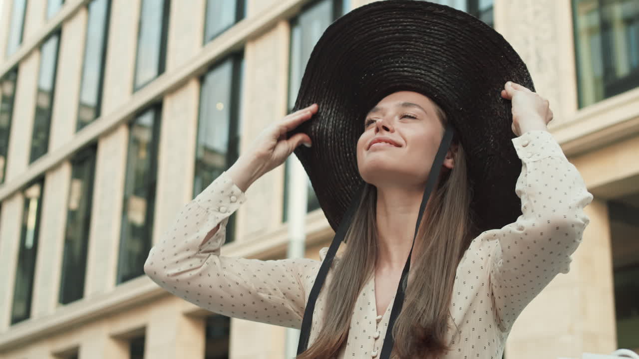 Woman Putting on Broad-brim Outside Building