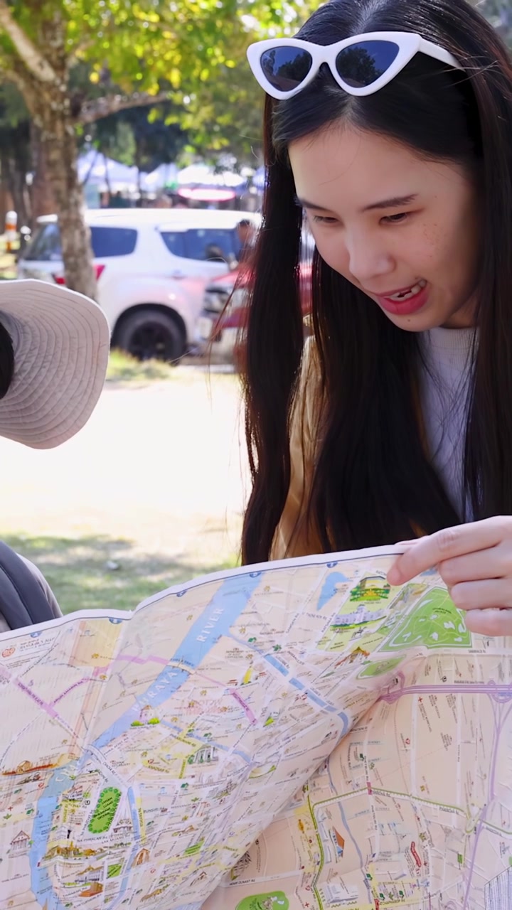 Thailandsk mor og ung søn studerer et papirkort sammen udendørs i klart naturligt sollys.