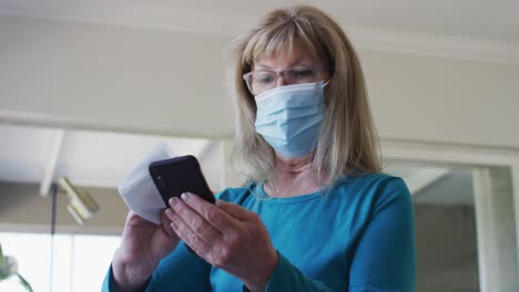 senior woman wearing face mask wiping her smartphone with a tissue