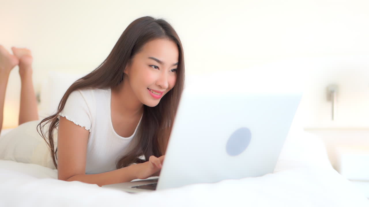 Young Pretty Asian Female on Bed Using Laptop For Communication to Other People. Modern Interaction Concept, Slow Motion