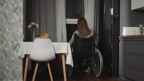 Pensive-woman-sits-near-kitchen-table-looking-out-window