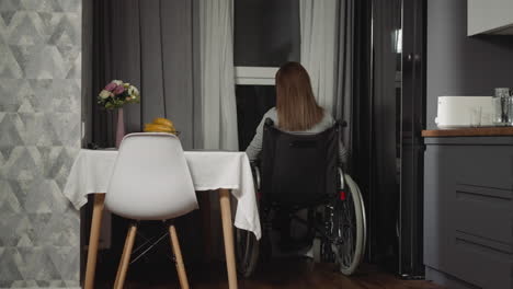 mujer pensativa se sienta cerca de la mesa de la cocina mirando por la ventana