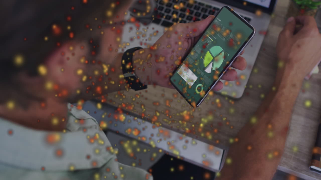 Data charts being animated on smartphone over desk, featuring smartwatch, laptop keys, particles