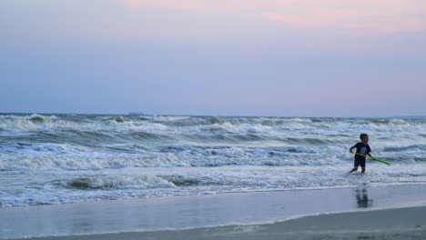 Little boy playing with water in the seashore. Cute child enjoys with his toy near the water in the evening. Happy childhood.