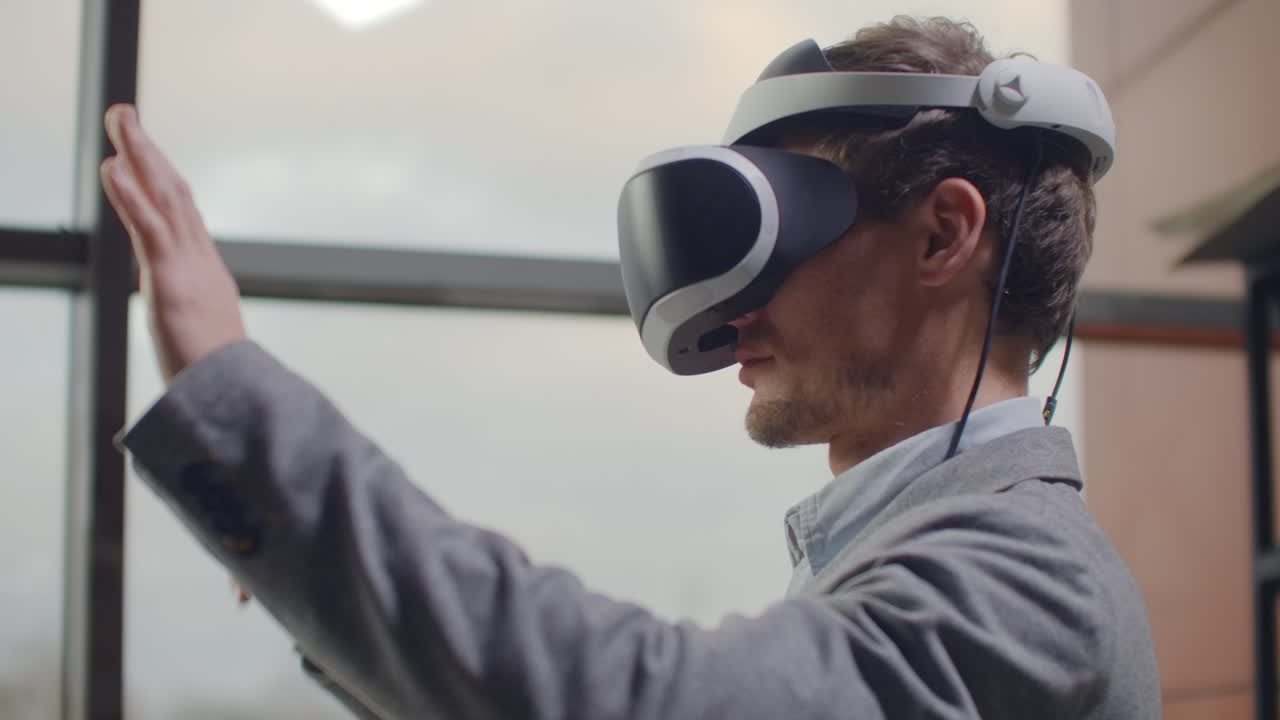 Portrait male architect-designer in a virtual reality helmet at in a modern office near a large window with his hands imitates the work of interface. Designing the future the concept of virtual architecture and design interface graphic applications.