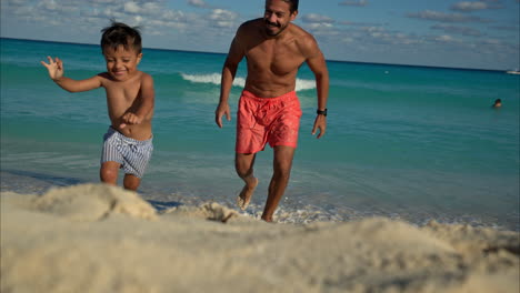 slow motion of a mexican latin brunette boy running away from his father at the beach being chased laughing and having fun in cancun
