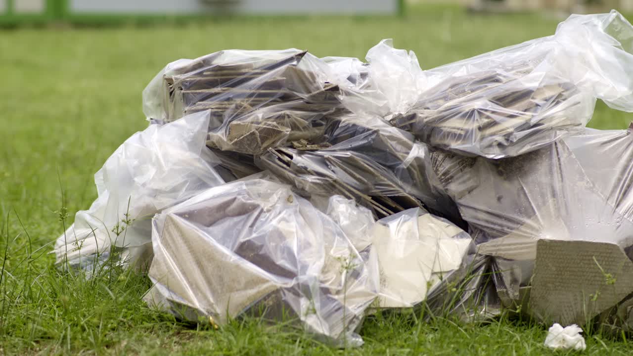 Pieces of asbestos material piled up in plastic bags on grass, poking out