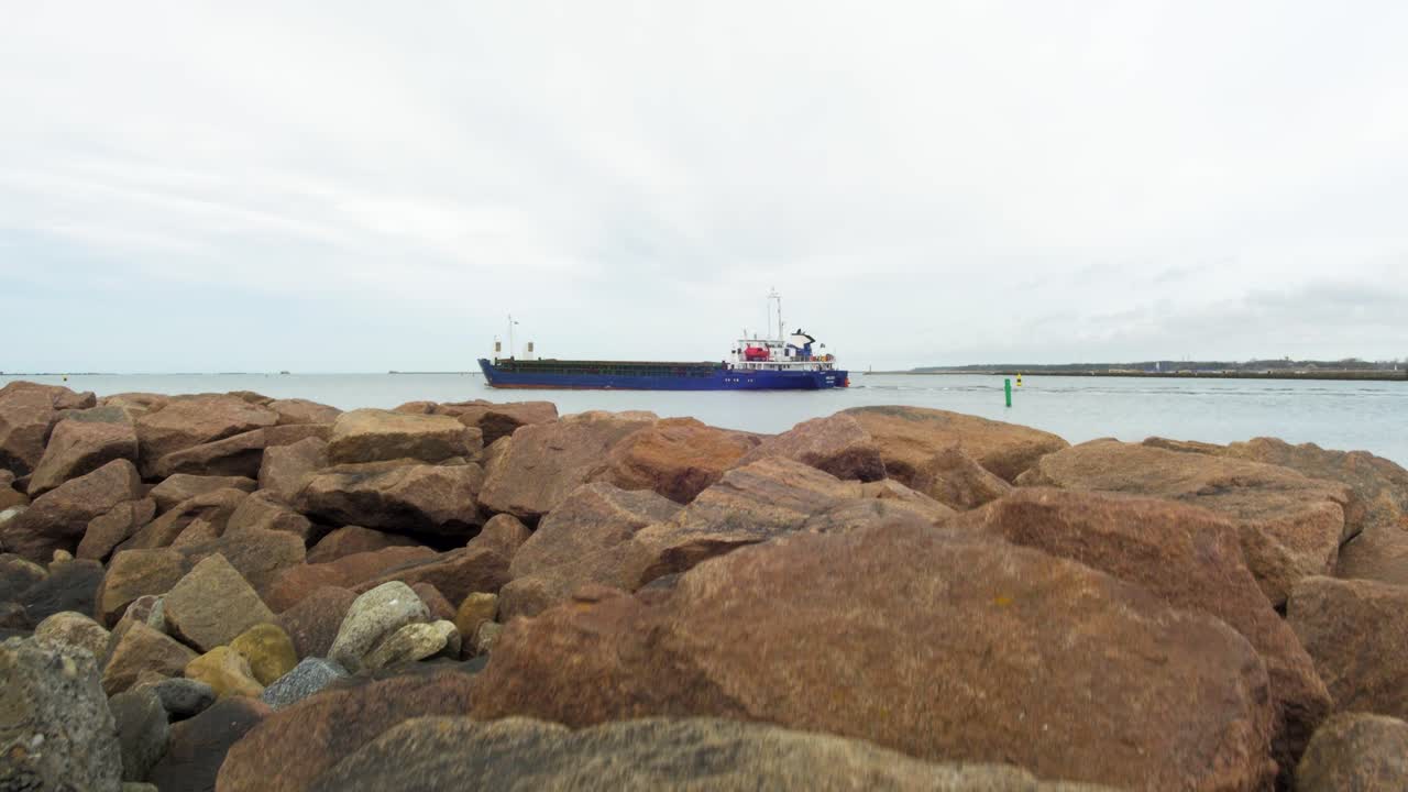 gran carguero azul que sale del puerto de liepaja , día de primavera nublado, amplio disparo revelador desde la inclinación hacia arriba desde las rocas del muelle de piedra