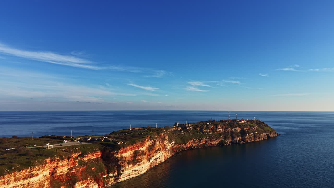 Vista costiera di un'isola rocciosa durante il giorno con cielo sereno sull'oceano e strutture distanti sulla terraferma