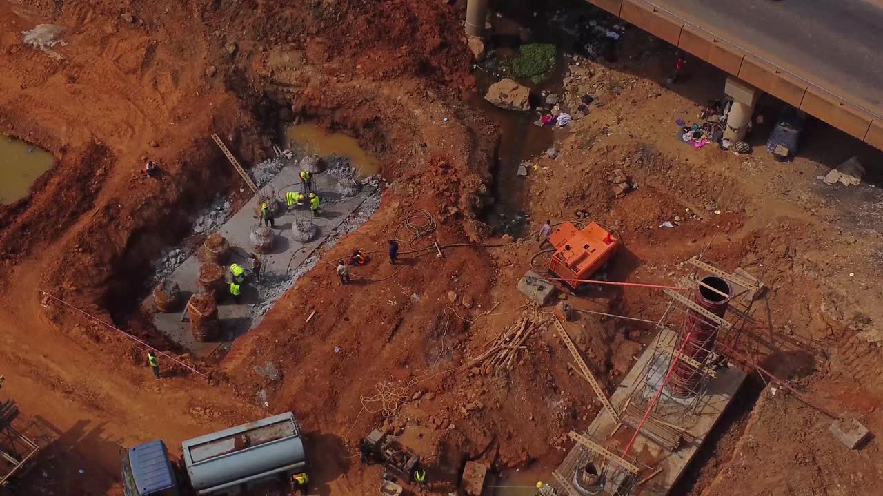 Vista aérea superior de trabalhadores da construção civil a edificar um grande pilar para uma ponte, como parte de uma autoestrada recém-desenvolvida em Abuja, Nigéria.