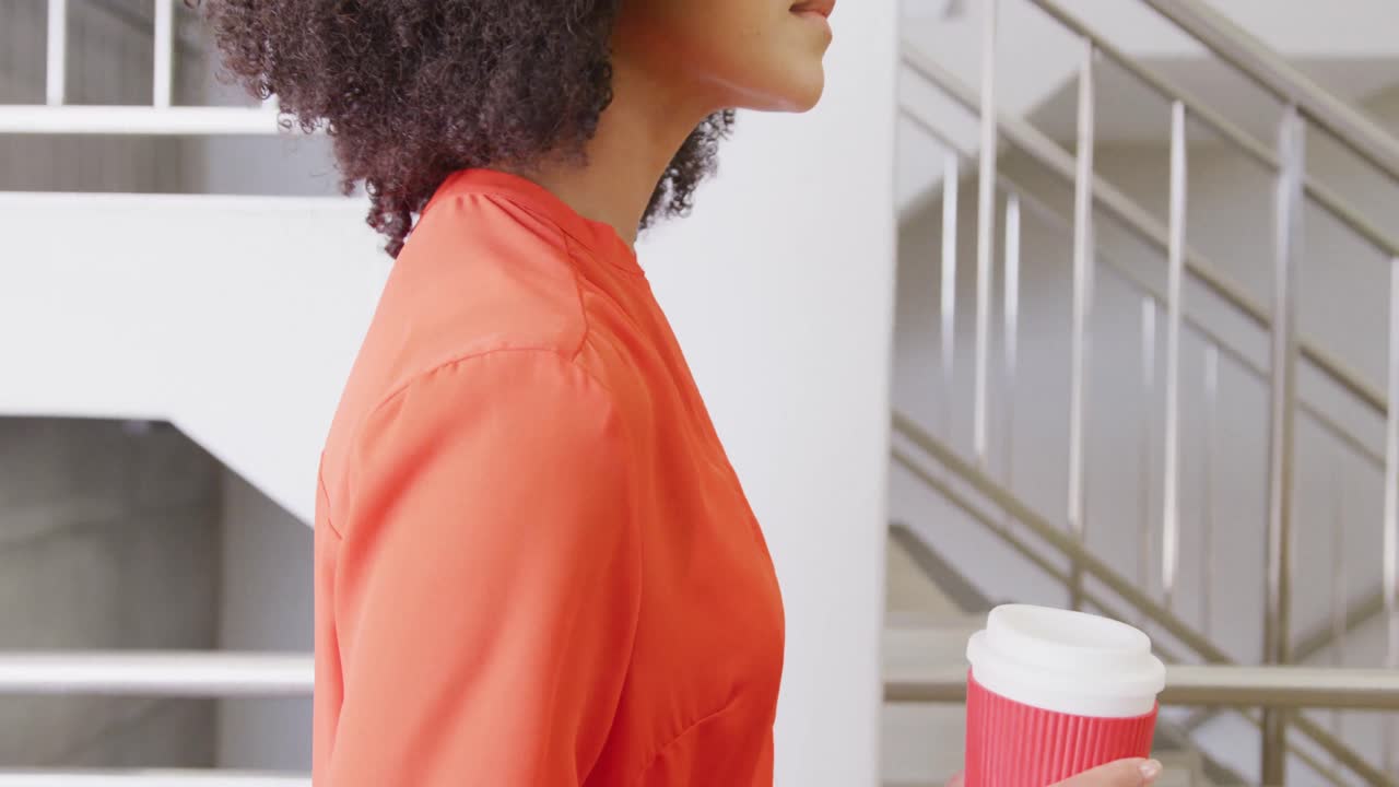 feliz hombre de negocios afroamericano subiendo las escaleras y sosteniendo café en la oficina, cámara lenta