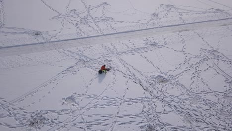 extreme slow panning aerial view of outdoorsman sitting next to freshly drilled hole while participating in ice fishing.