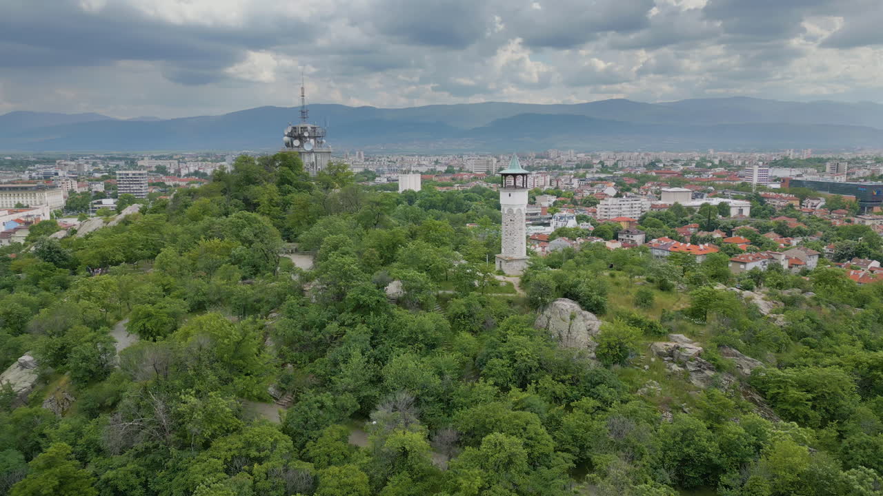 Aerial orbit shot of the iconic clock tower on Sahat Tepe hill in Plovdiv, Bulgaria. Springtime landscape under dramatic sunset clouds with panoramic view of the city
