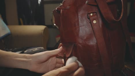 a person wiping off the dirt on the outer part of brown leather backpack - closeup shot