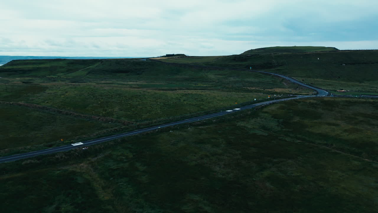 그 위에 몇 대의 차량과 배경의 언덕이 있는 도로 경로, 아일랜드의 모헤르 절벽에서 촬영된 공중 드론