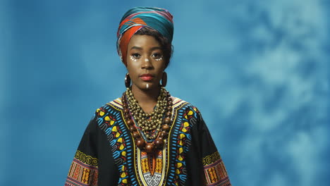 african american young woman in turban and make-up looking with serious expression at camera